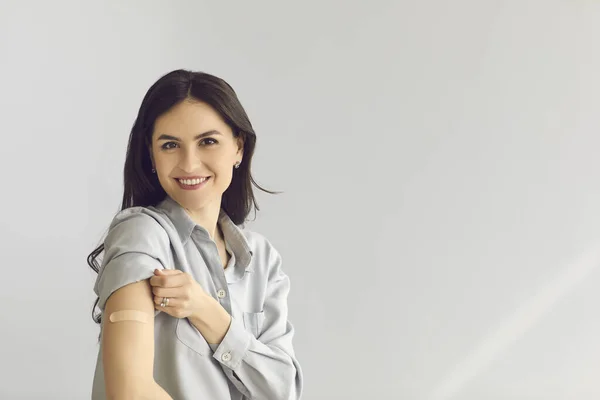 Mujer joven en el espacio de copia fondo sonriendo y mostrando el brazo después de la inyección de la vacuna — Foto de Stock