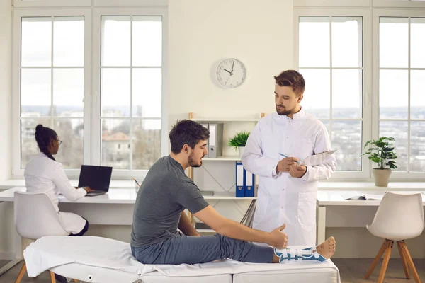 Arzt und Patient mit gebrochenem Bein bei Untersuchung auf Verletzung im Krankenhaus — Stockfoto