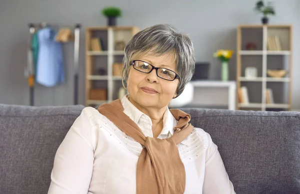 Portrait de femme mature dans des lunettes assis sur le canapé à la maison et regardant la caméra — Photo