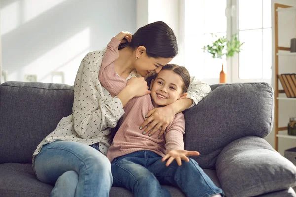 Vrolijke jonge moeder en dochter veel plezier, spelen en knuffelen terwijl thuis zitten op de bank. — Stockfoto