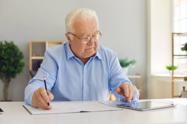 Yaşlı bir işçi internetten bilgi topluyor ve not defterine yazıyor.