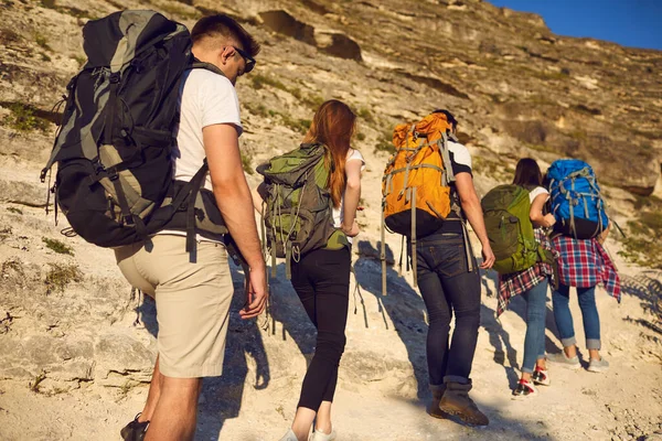 Grupo de jovens caminhantes com mochilas sobe uma trilha de montanha em um dia ensolarado. — Fotografia de Stock