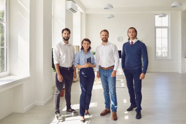 gülümseyen iş ortakları veya proje ekibi modern ofiste durup kameraya bakıyor