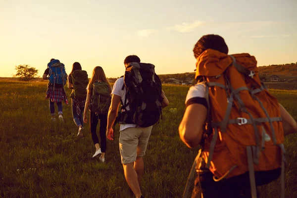 Grupo de viajantes com mochilas andando em um único arquivo no campo durante as férias de verão ativas — Fotografia de Stock