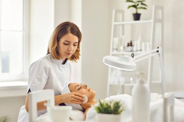 Genç kozmetolog ya da dermatolog kaplıcada yalancı kadınların yüzünü pamukla temizliyor.