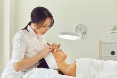 Kadın dermatolog cilt muayenesi sırasında kadınların alnına dokunuyor.