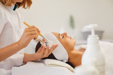 Güzellik uzmanının elleri nemlendirici maske ve fırçayla kavanozu tutuyor.