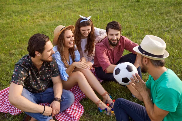 Nyári szünet. Barátok kommunikálnak focimeccs után a természetben. Férfiak és nők beszélnek és nevetnek vidéken — Stock Fotó