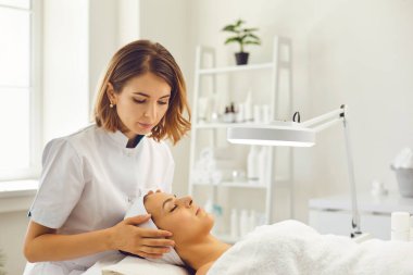 Güzellik uzmanı, yüz dolaşımını geliştirmek için genç bir kıza hafif bir yüz masajı yapıyor.