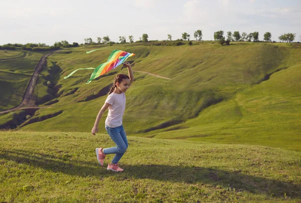 Seorang gadis kecil dengan layang-layang berjalan di atas bukit di alam di musim panas. — Stok Foto