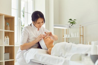 Kadın dermatolog cilt muayenesi sırasında kadınların alnına dokunuyor.