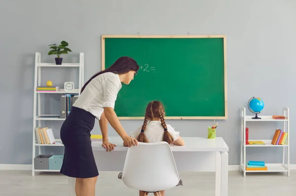 Жінка-вчителька допомагає маленькій дівчинці на уроці математики в класі. Репетитор і учень, які працюють разом під час занять у школі — стокове фото