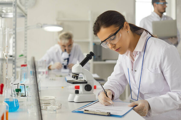 Young woman scientist making notes in report working at chemistry laboratory