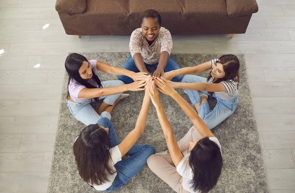 Diverso gruppo di giovani donne felici sedute in cerchio sul pavimento, che si tengono per mano e sorridono — Foto Stock