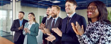 Group of business people celebrates success by applauding during a meeting, presentation, or event in the office. The scene captures the excitement and teamwork within a corporate environment.