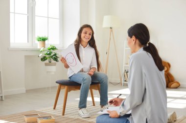 Don t be afraid to talk about emotions. Happy teen girl in meeting with professional child psychologist talks about emotions. Cheerful girl shows female psychologist painted smiling smiley.