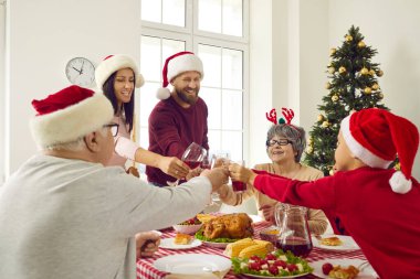 Noel Baba şapkalı güzel mutlu aile Noel 'i süslü bir masada kutluyor. Kırmızı şarap için, kadeh tokuşturun ve Noel tatili için birbirinizi tebrik edin..