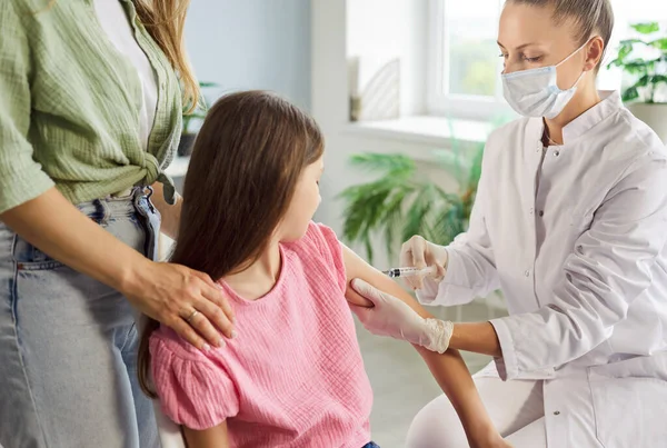 Child receives vaccination injection from doctor. A nurse uses a syringe to vaccinate the patient arm during medical clinic visit, emphasizing careful healthcare. Kids vaccines keep children safe.