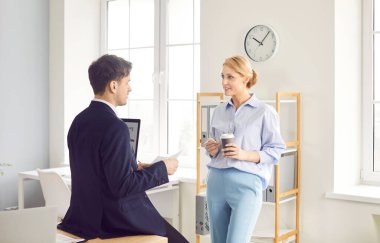 Positive business colleagues engaged in conversation or discussion and resting during a break in the office, enjoying coffee together. Teamwork and the collaborative atmosphere of the workplace.