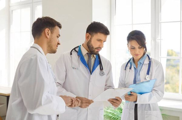 Medical gathering talk, council of physicians, doctors discussion using paper documents, sharing with interns or younger female colleague, discussing patient diagnosis, proposing treatment plan