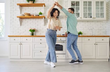 Happy couple dancing together at home, smiling. In a modern kitchen they laugh and sway, sharing happiness, romance, and a trusting relationship. Warm unity, love, lifestyle, and fun concept.