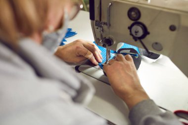 Shoe factory worker using an industrial sewing machine to make a detail for new footwear, needle and hands holding shoe detail in closeup, view over shoulder. Footwear manufacturing industry concept