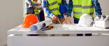 Professional builders discussing architect project at construction site. Construction engineers, architect working on blueprint architectural project at meeting. Building, renovation, remodeling