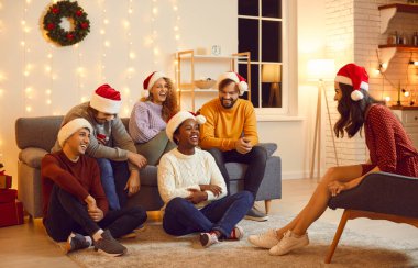 Happy diverse young people relax at home celebrate New Year holidays together. Smiling multiracial millennial friends laugh and joke enjoy Christmas celebration. Winder vacation concept.