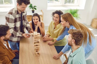 Top view portrait of a group of happy young friends students guys and girls playing together in board game with wooden building blocks at home and enjoying time together sitting at the table.
