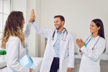 Hastane ofisindeki doktorlar ve hemşireler de dahil olmak üzere kendini işine adamış bir sağlık ekibi. Gülümsemeler beşlik çakarken yüzleri aydınlatıyor, işbirliği ve başarıları kutluyorlar..