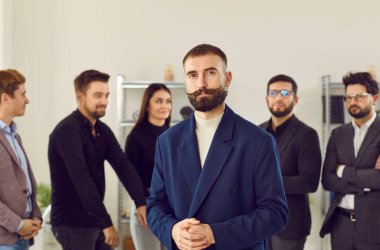Business colleagues standing together with businessman leader on foreground. Portrait of confident stylish leader with hipster mustache looking at camera with partners behind
