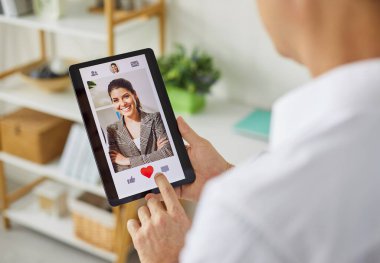 Bir kişinin akıllı telefon flört uygulaması kullanarak bir oturma odasında bir kullanıcı profili gibi kalp simgesini tıklatarak ekranı ve parmak etkileşimini göstermesi. Aşkı ve online randevu kavramını bul.