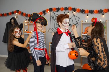 Face paint artist doing creative spooky makeup for kids at fun Halloween party at home. Team of little children getting facepaint applied before they are ready to go trick or treating all together