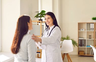 Friendly woman doctor supporting her female patient during medical examination in hospital. Smiling lady in white coat talking to young woman, calming her down and telling about effective treatment