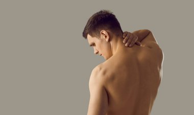 Naked young man on grey studio background suffer from neck ache. Pain in upper back. Unwell sick guy struggle with backache have muscle spasm or nerve inflammation from incorrect posture.