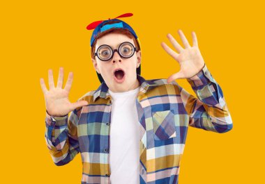 Studio shot of very surprised child. Portrait of little school boy wearing plaid shirt, round glasses and funny propeller cap looking at camera with shocked, astonished facial expression
