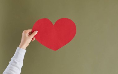 Close up of person hand isolated on green studio background show red heart sign or symbol demonstrate love and care. Woman express affection feel thankful grateful. Charity, volunteer concept.