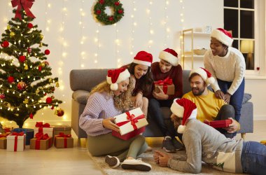 Smiling diverse multiracial friends celebrate Christmas holidays together open presents. Happy international people have fun on New Year eve unpack gifts at winter vacation celebration indoors.