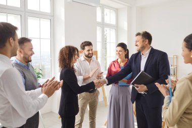 Ofisteki meslektaşlar toplantı sırasında başarılı bir anlaşmayı kutluyorlar. El sıkışma, takım çalışmasını, ortaklığı ve zaferi, iş birliği ve güvenlerini güçlendirmeyi simgeler..