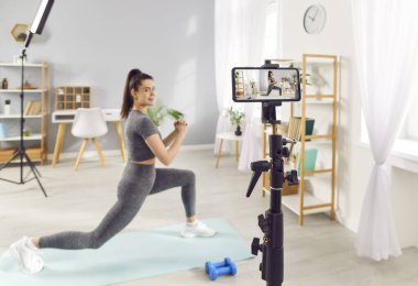 Mutlu kadın evde çalışırken kendini kaydediyor. Spor eğitmeni çevrimiçi içerik yaratıcısı etkileyicisi video bloğu ve web fitness rutin dersini çekerek ileri doğru hamle yapıyor