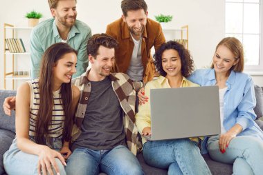 Mutlu öğrenci portresi kanepede oturup dizüstü bilgisayarda komik filmler seyrediyor ya da evde oturup gülüyor. Genç erkekler ve kızlar birlikte vakit geçirmekten zevk alıyorlar..