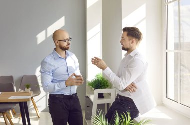 Modern ofiste dikilirken konuşan iki odaklı erkek arkadaş. İş adamı iş arkadaşıyla iletişim kuruyor, sohbet ediyor, projeyi tartışıyor ve fikirleri paylaşıyor ya da gündelik sohbetler yapıyor.