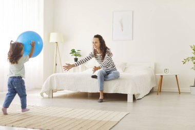 Yatakta oturmuş gülümseyen genç anne kızına sarılmak ya da spor salonuna gitmek için ellerini uzatıyor. Neşeli bir aile, anne ve çocuk birlikte eğleniyor ve yatak odasında oynaşıyorlar. Aile aktiviteleri