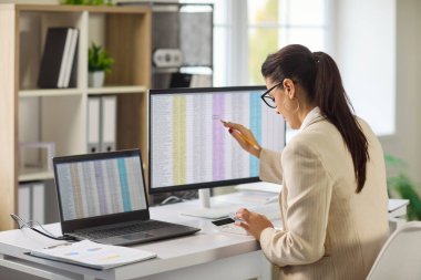 Muhasebeci ofis bilgisayarında denetim analizi yapar. Kadın hesap çizelgesini gözden geçirir, hesap makinesi kullanır, doğruluğu ve makama uyumu onaylar. Açık konsept finans denetimi ve raporlama.