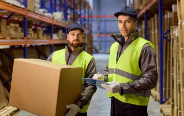 Depo çalışanlarının envanter paketleri takım çalışmasıyla dolu. İki yükleme işçisi, bir depoda nakliye ve lojistik teslimat için stokları kontrol ediyor. Envanter denetimi kavramı.