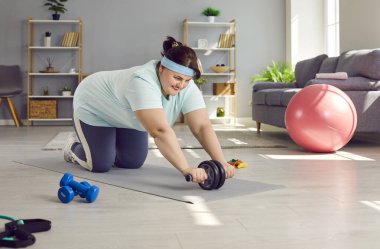 Mutlu, şişman, tombul, tombul, kilolu, kilolu, artı beden ölçülerinde, evde oturma odasında spor yaparken kas silindiri ile spor yapan genç bir kadın.