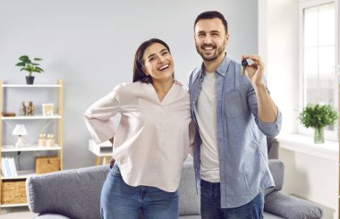 Oturma odasında, yeni modern dairelerinin anahtarlarını alan mutlu aile çiftlerine kucak açıyoruz. Anahtar evli çiftte. Yeni evlerini alan genç bir çift. Emlak, mülk.