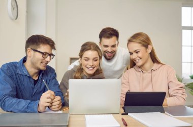 Bir grup mutlu yaratıcı üniversite öğrencisi masada oturuyor, modern dizüstü bilgisayarlara bakıyor, konuşuyor, iş fikirlerini tartışıyor, birlikte web pazarlama sunumu yapıyorlar. Eğitim kavramı