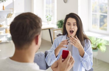 Kırmızı hediye kutusu olan genç adam mutlu sevgilisine evlenme teklif ediyor. Oturma odasında duruyor. Erkek kişi, güzel kız arkadaşına nişan yüzüğü ya da mücevherle sürpriz hediye veriyor..