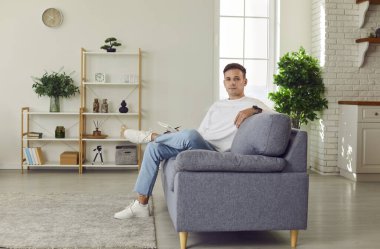 Evdeki yakışıklı bekar adam rahatlamak için yeni kanepesinde dinleniyor, rahat bir evde güzel bir hafta sonu geçiriyor, ev sahibi taşınıyor, mobilyaların üzerinde oturuyor, düşünüyor, modern oturma odasında kafa yoruyor.